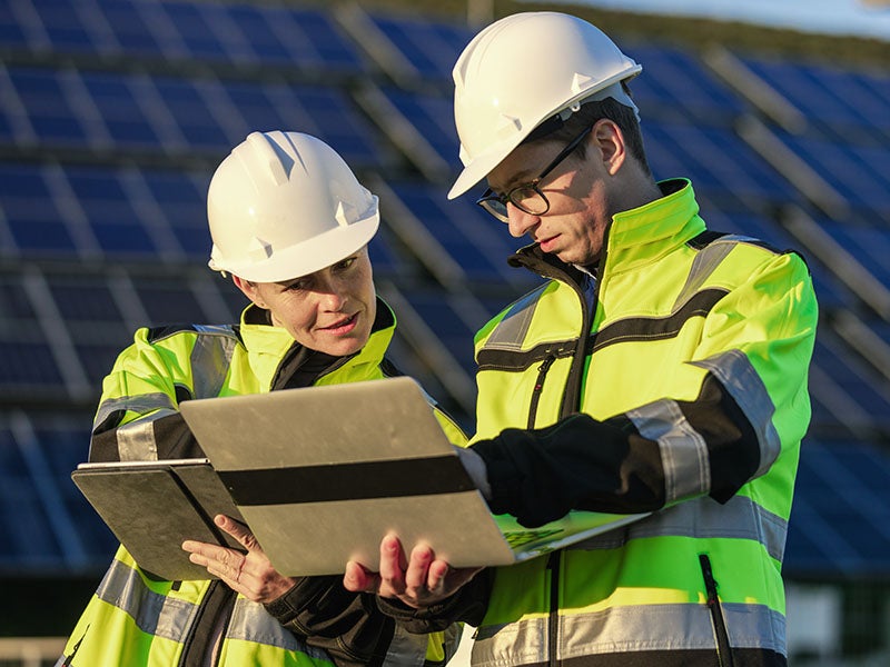 Two engineers doing a routine inspection of a solar power plant using digital tablet and laptop. Alternative energy concept